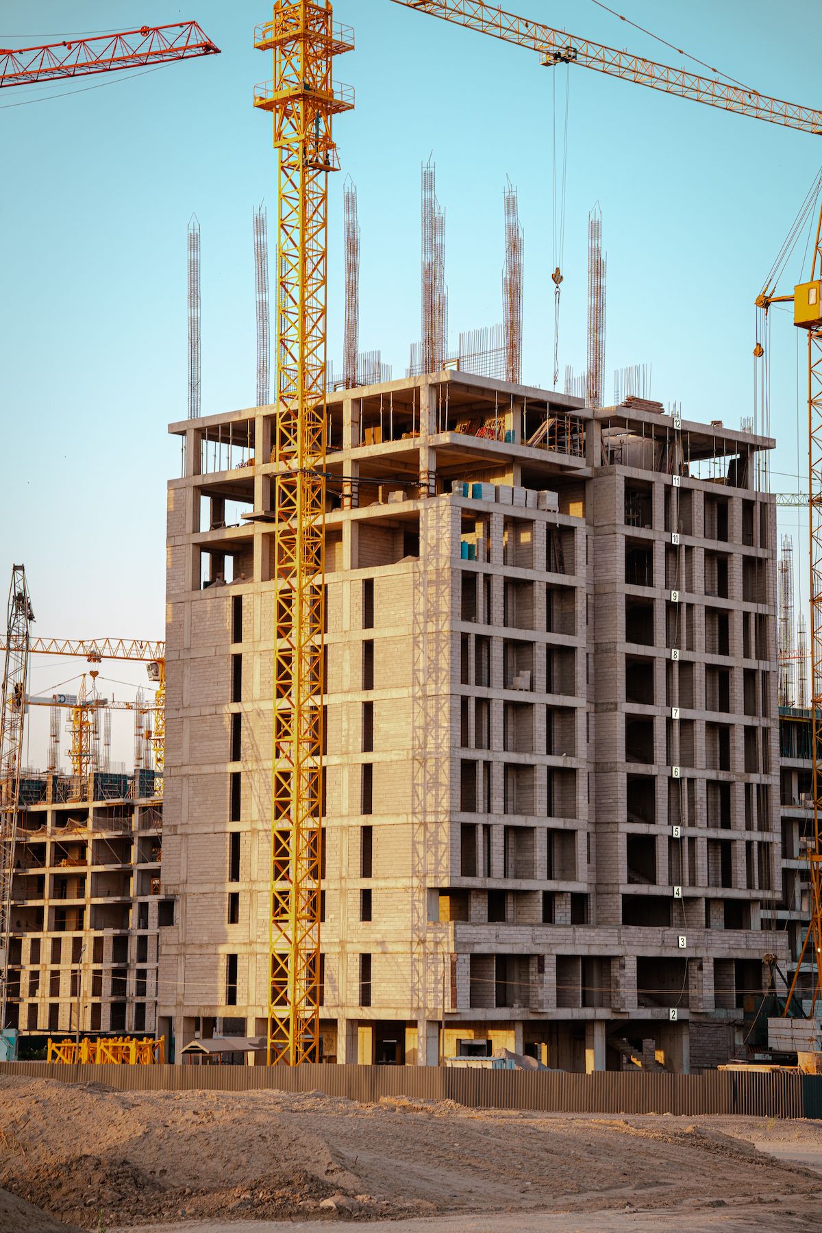 Construction site with cranes and an unfinished building against a clear sky during sunset.